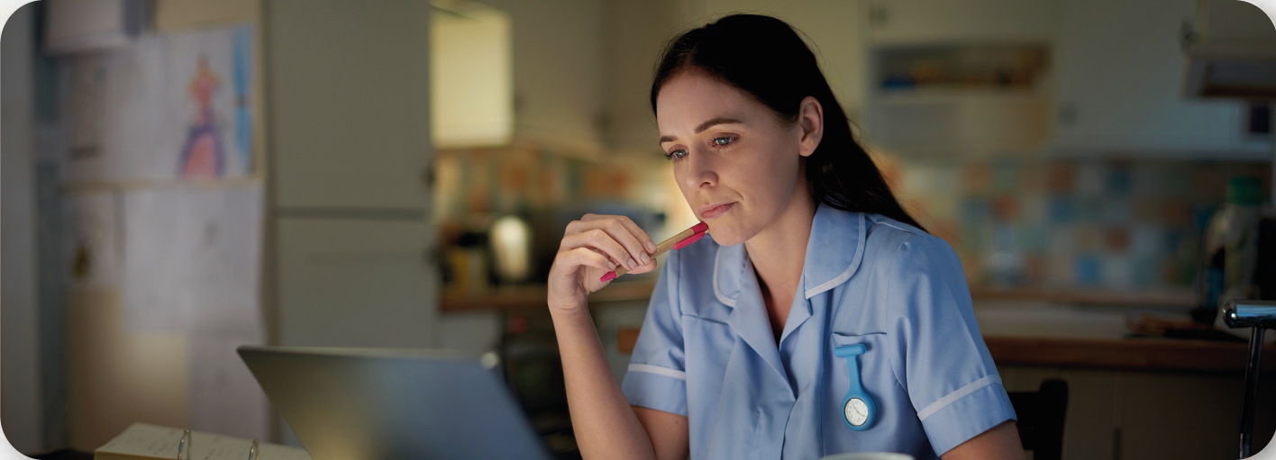 Carer with pen by chin looking at a computer